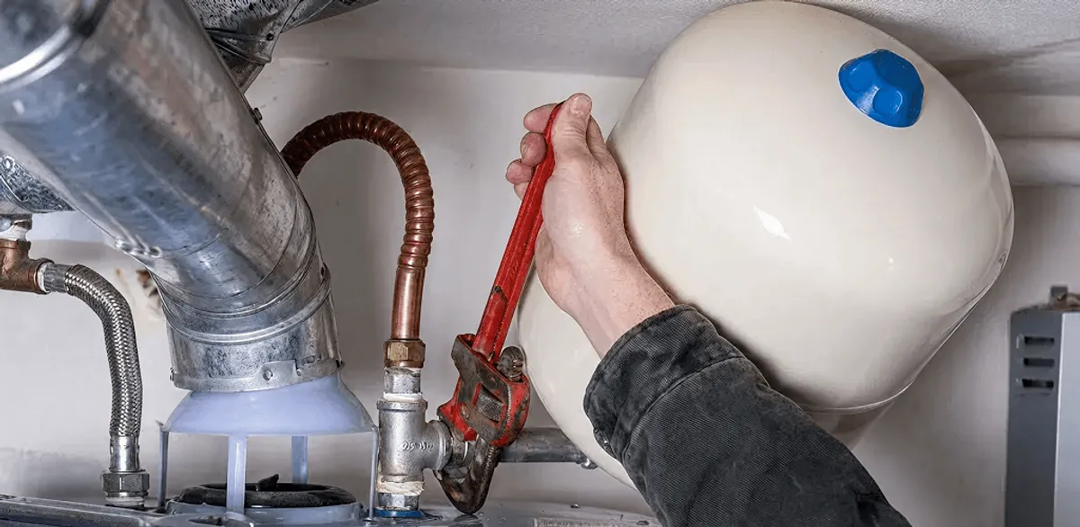 Water heater repair technician tightening plumbing connections near a tank unit in Riverside, CA